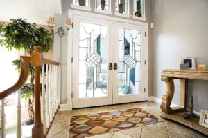Bright Southern California foyer with glass double doors, colorful geometric rug, potted plant, and console table with framed photos.