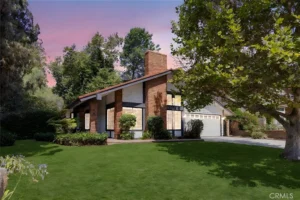 A modern house with a sloped roof and brick walls, surrounded by green plants, with a pink sky at sunset.