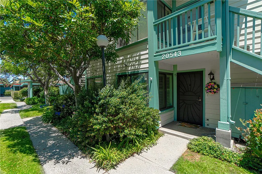 Green-trimmed townhouse with a welcoming entrance, trees, shrubs, staircase, and hanging flower basket.