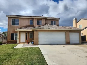 Two-story beige Southern California house with three-car garage, tiled roof, white windows, and a trimmed lawn.